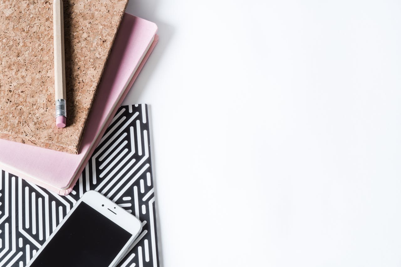 why-choose-us Stylish flat lay of a creative workspace with notebook, pencil, and smartphone on a white background.