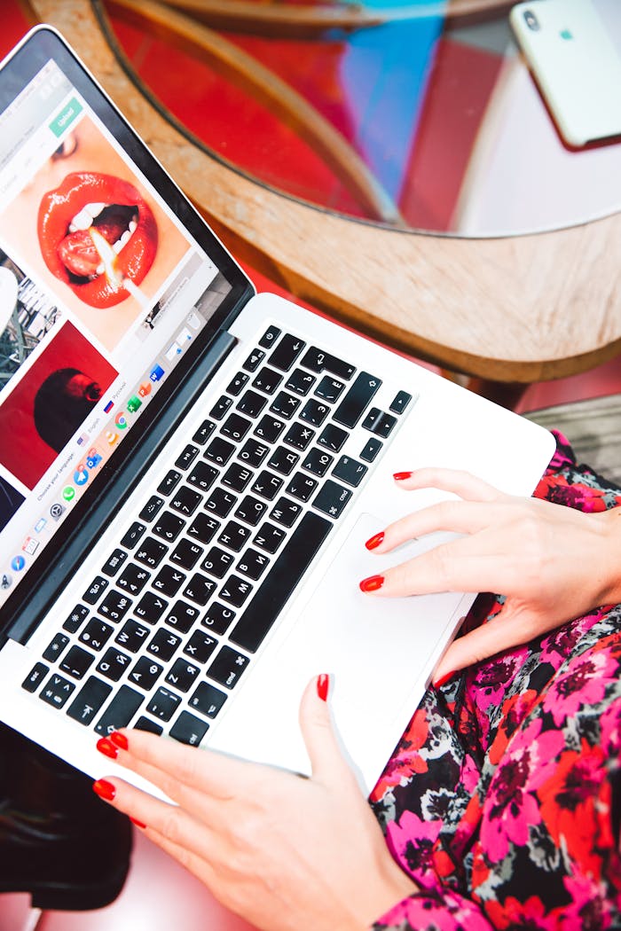 A woman with red nails works on a laptop browsing fashion websites, showcasing online trends.